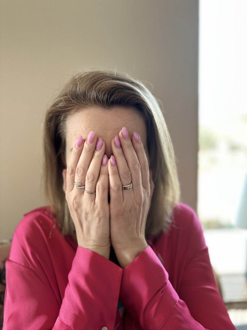 Lenka Tarpataki si v růžové košili zakrývá obličej rukama, fotka vyjadřuje stres, zahlcení a bezmoc.